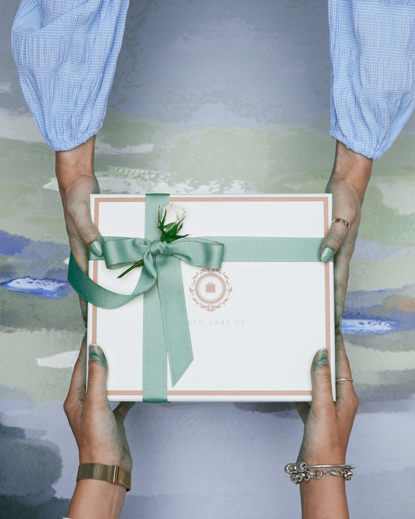 Un coffret cadeau noué d’un ruban vert, tendu à deux mains